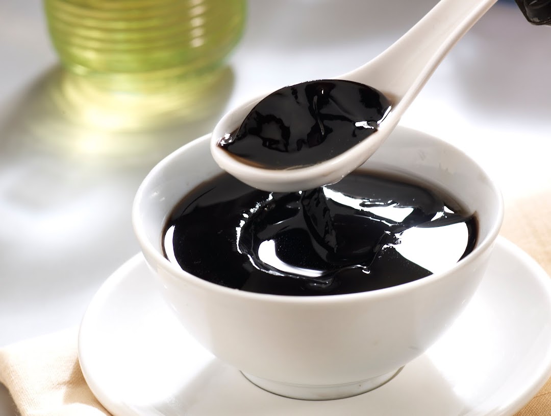 A close-up of a bowl of traditional black herbal jelly dessert being served with a spoon.