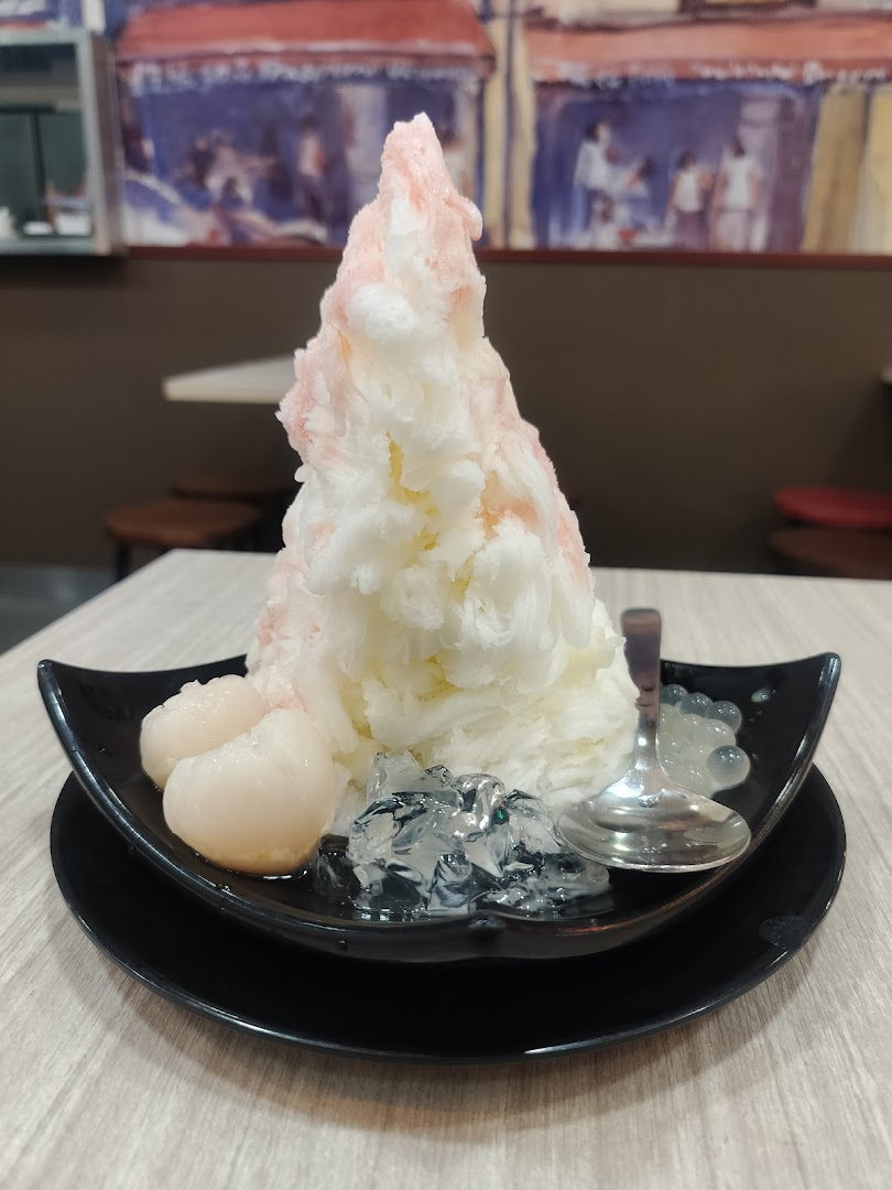 A towering shaved ice dessert with lychee and jelly toppings in a black bowl.