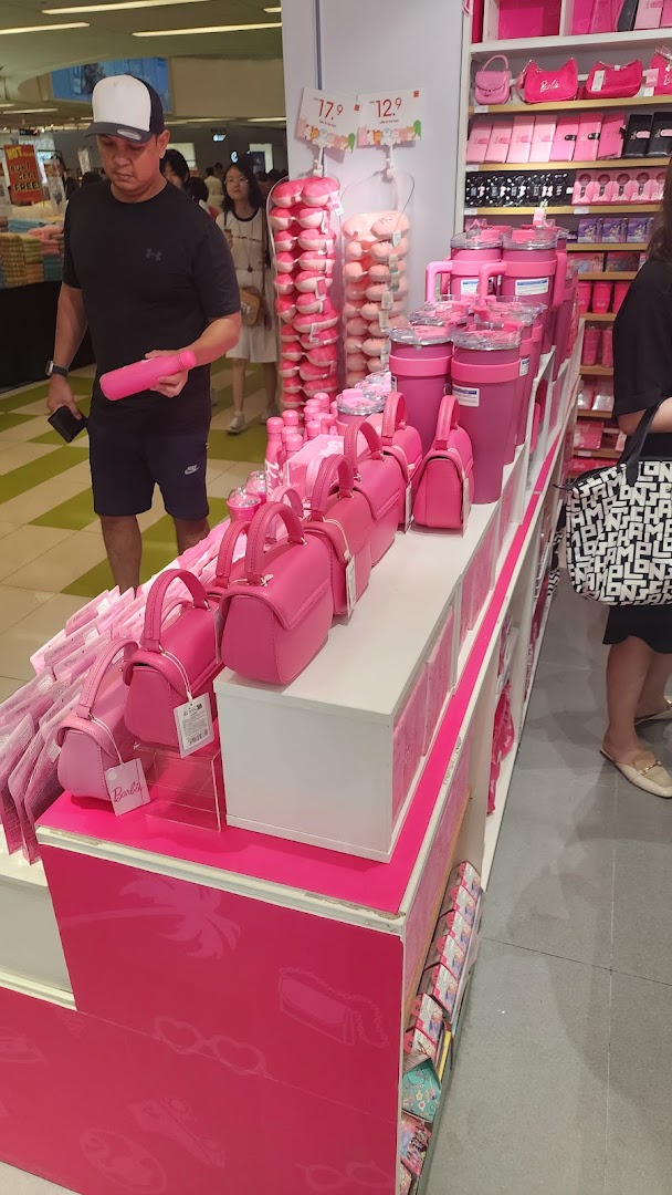 A vibrant display of pink Barbie-themed products, including bags and bottles, inside a MINISO store.