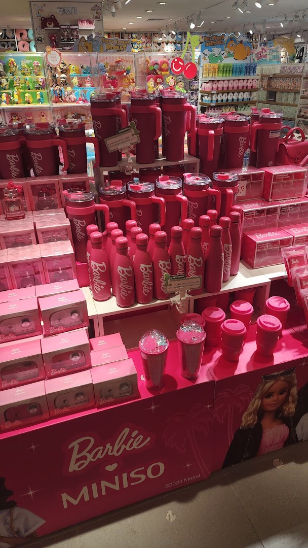 A vibrant display of pink Barbie x MINISO collaboration products, including bottles and tumblers, inside the store.