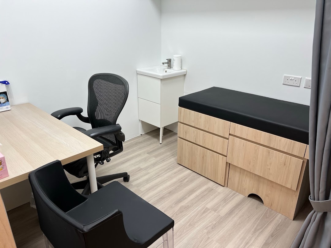 A clean and well-equipped medical examination room with a desk, chair, sink, and examination bed.