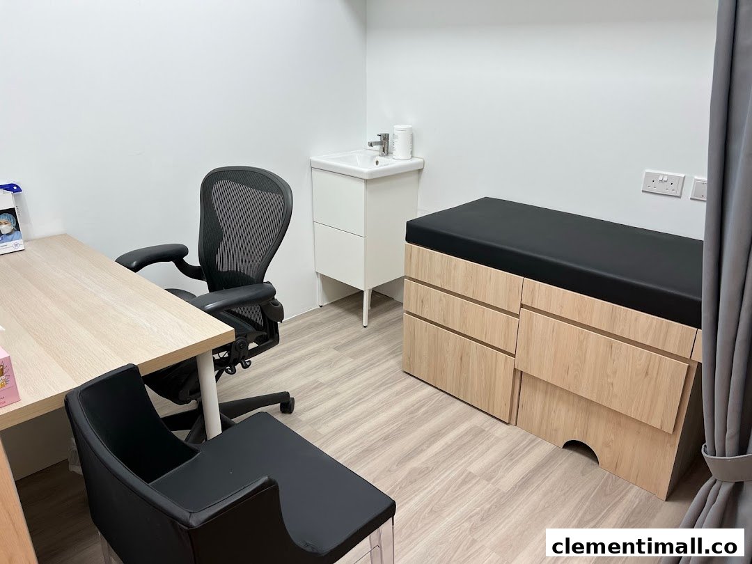 A clean and well-equipped medical examination room with a desk, chair, sink, and examination bed.