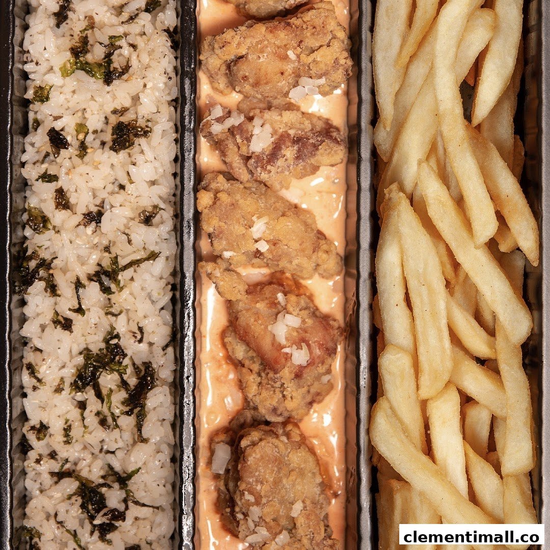 A close-up of a bento box featuring fried chicken, seaweed rice, and golden fries.