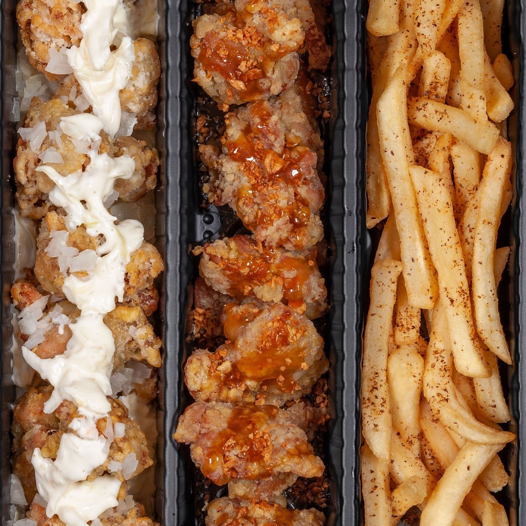 Close-up of fried chicken pieces with various toppings and a side of seasoned fries in a tray.