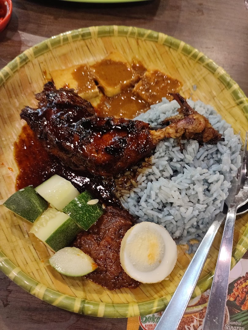 A vibrant plate of Nasi Kerabu with grilled chicken, blue rice, tofu, cucumber, and a boiled egg.