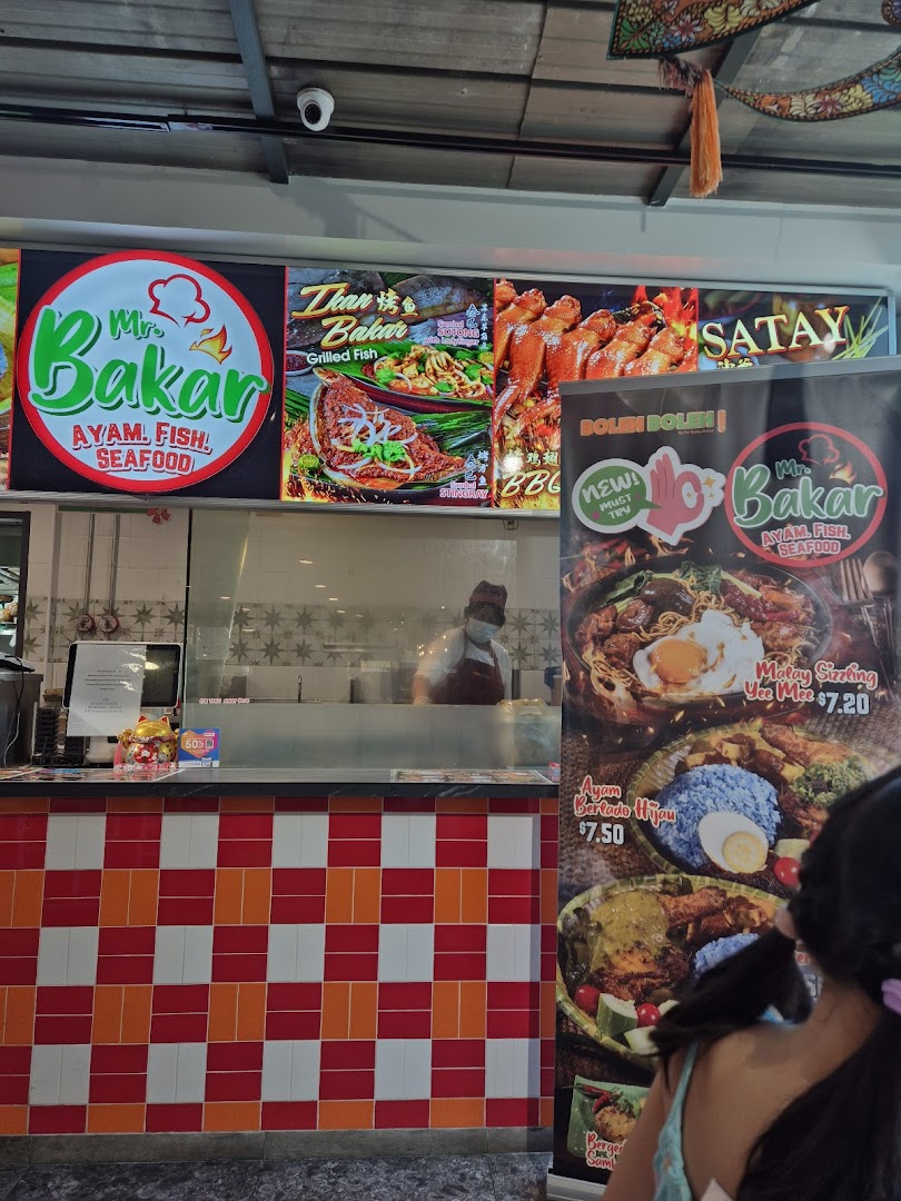 A vibrant food stall counter at Mr Bakar, showcasing grilled dishes and specific menu items with prices.
