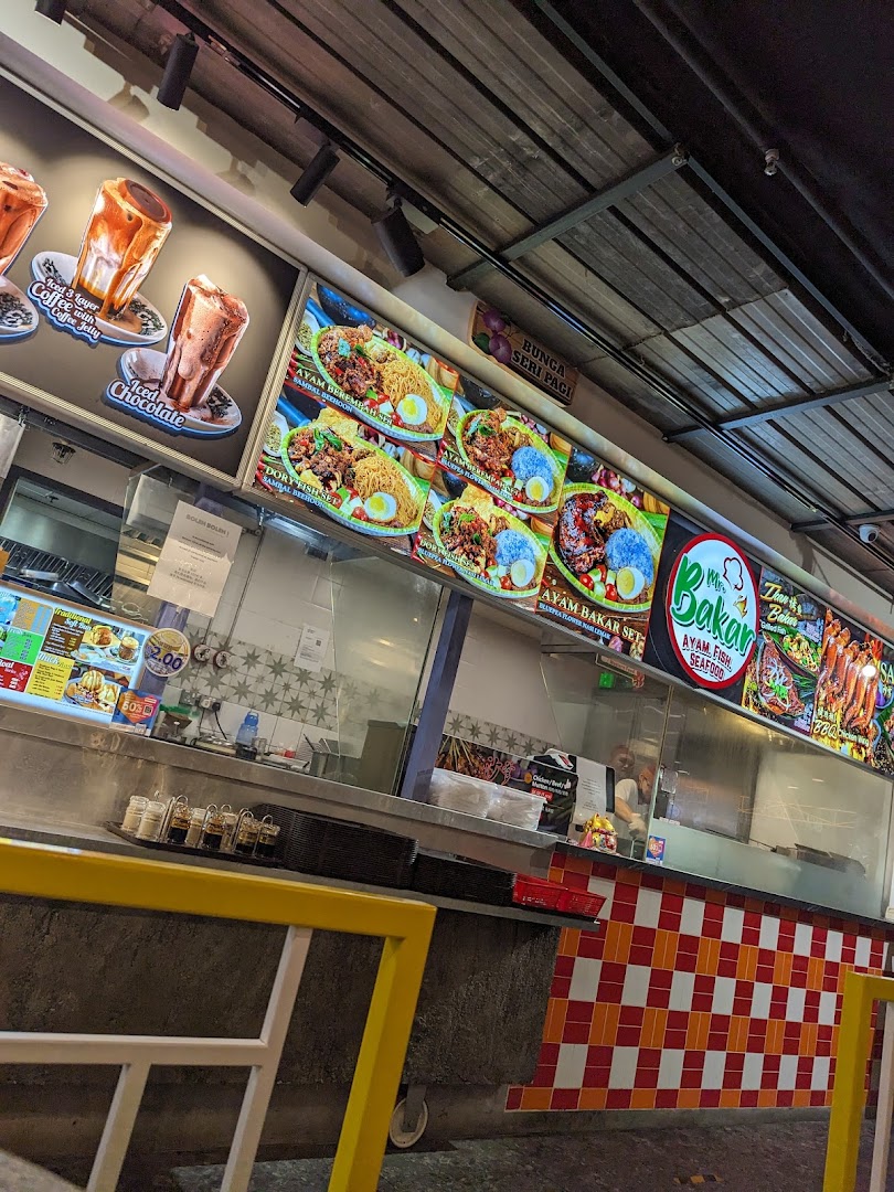 The counter of Mr Bakar food stall featuring large digital menu boards displaying various Malay and seafood dishes and drinks.