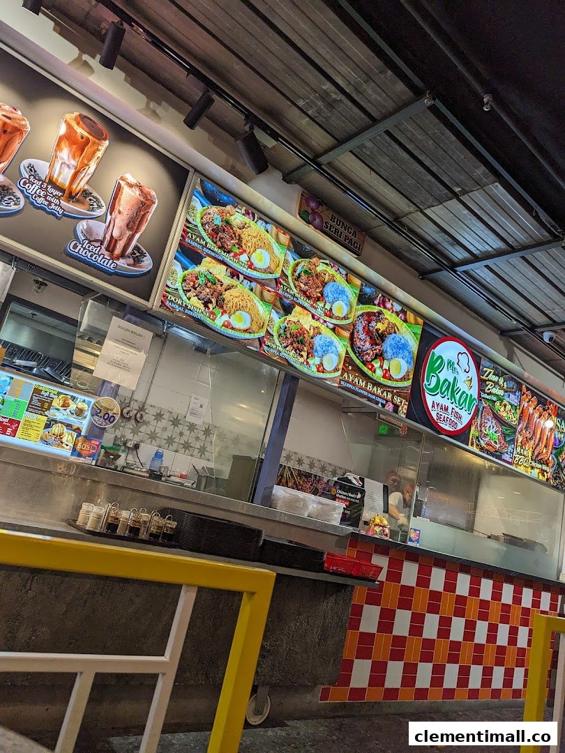 The counter of Mr Bakar food stall featuring large digital menu boards displaying various Malay and seafood dishes and drinks.