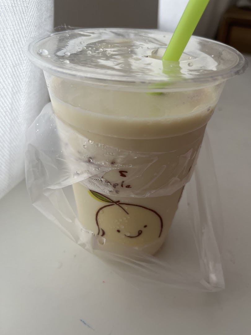 A refreshing light-colored drink in a plastic cup with a green straw and a cute fruit design.