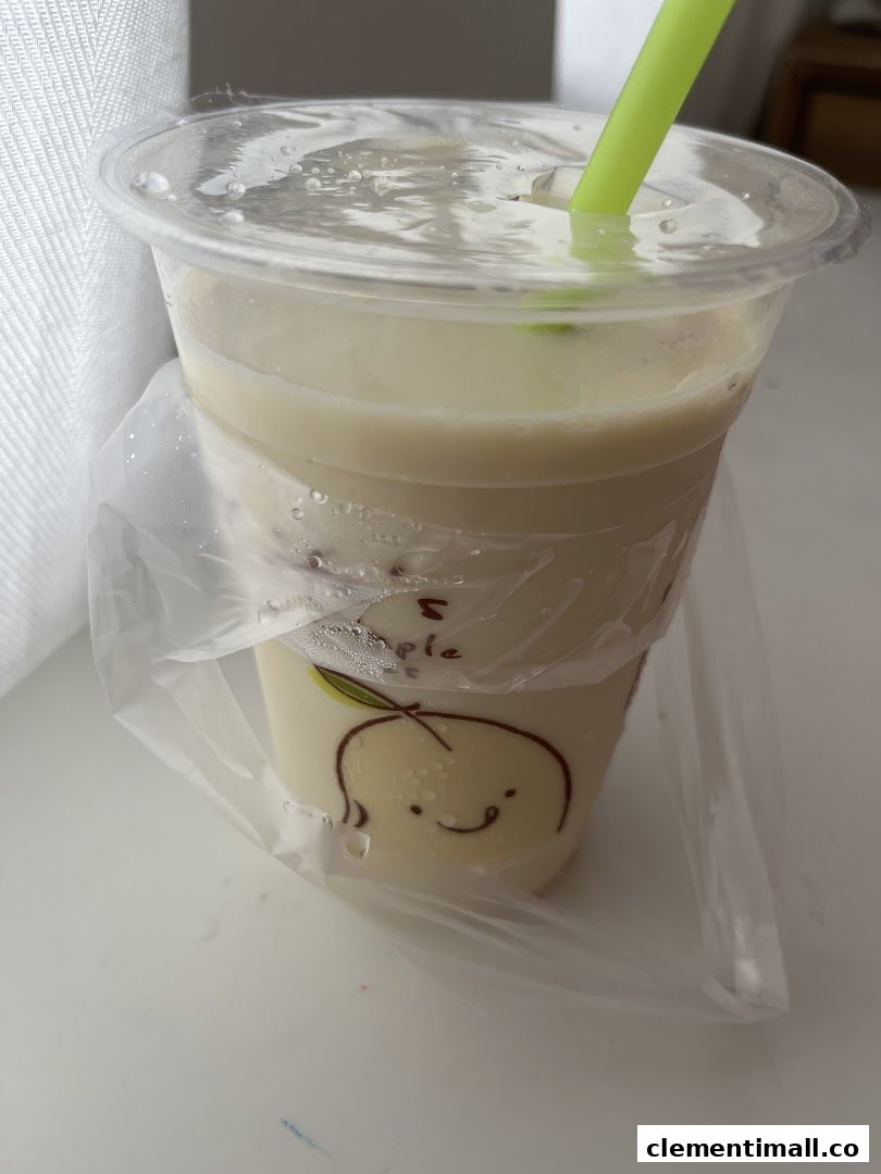 A refreshing light-colored drink in a plastic cup with a green straw and a cute fruit design.