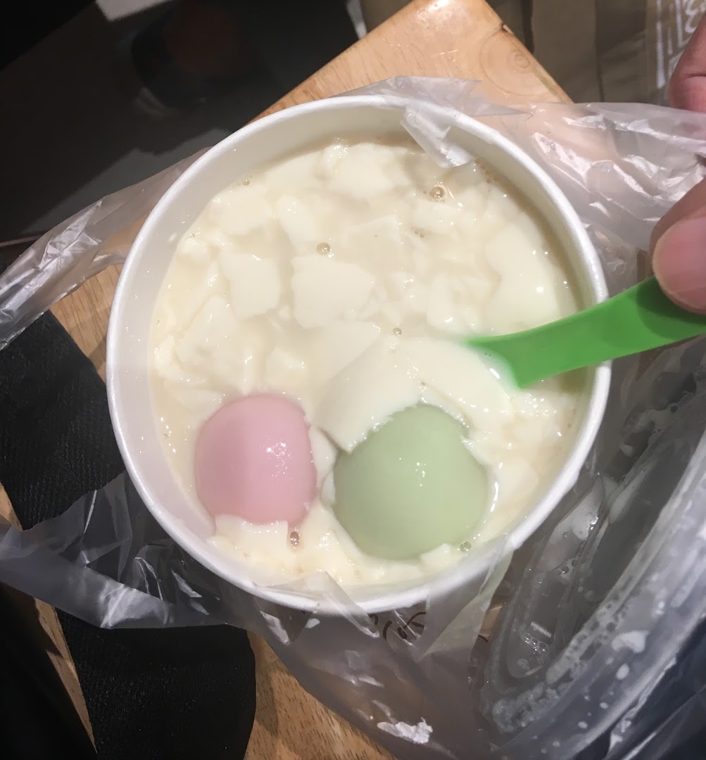 A close-up of Mr Bean's signature beancurd dessert with colorful tangyuan, being enjoyed with a spoon.