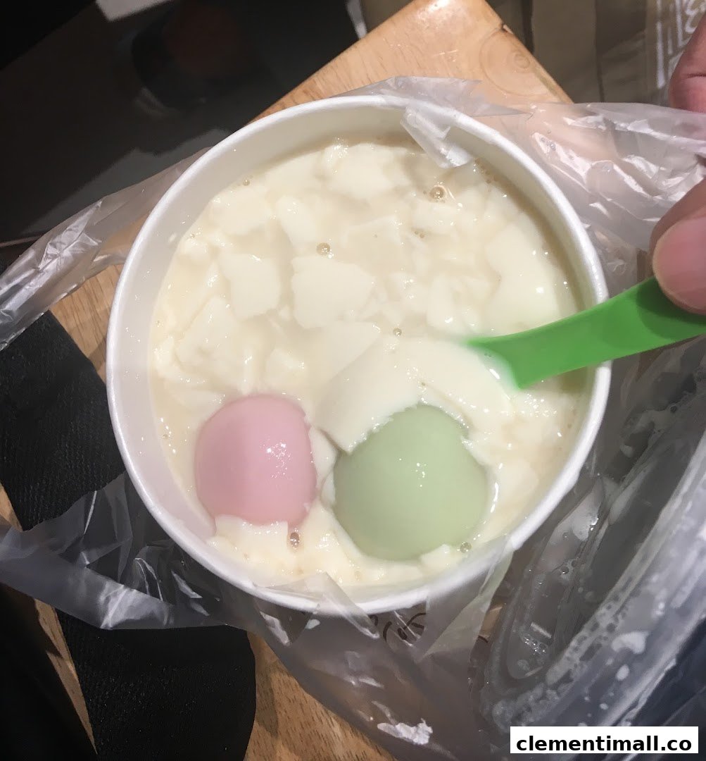 A close-up of Mr Bean's signature beancurd dessert with colorful tangyuan, being enjoyed with a spoon.