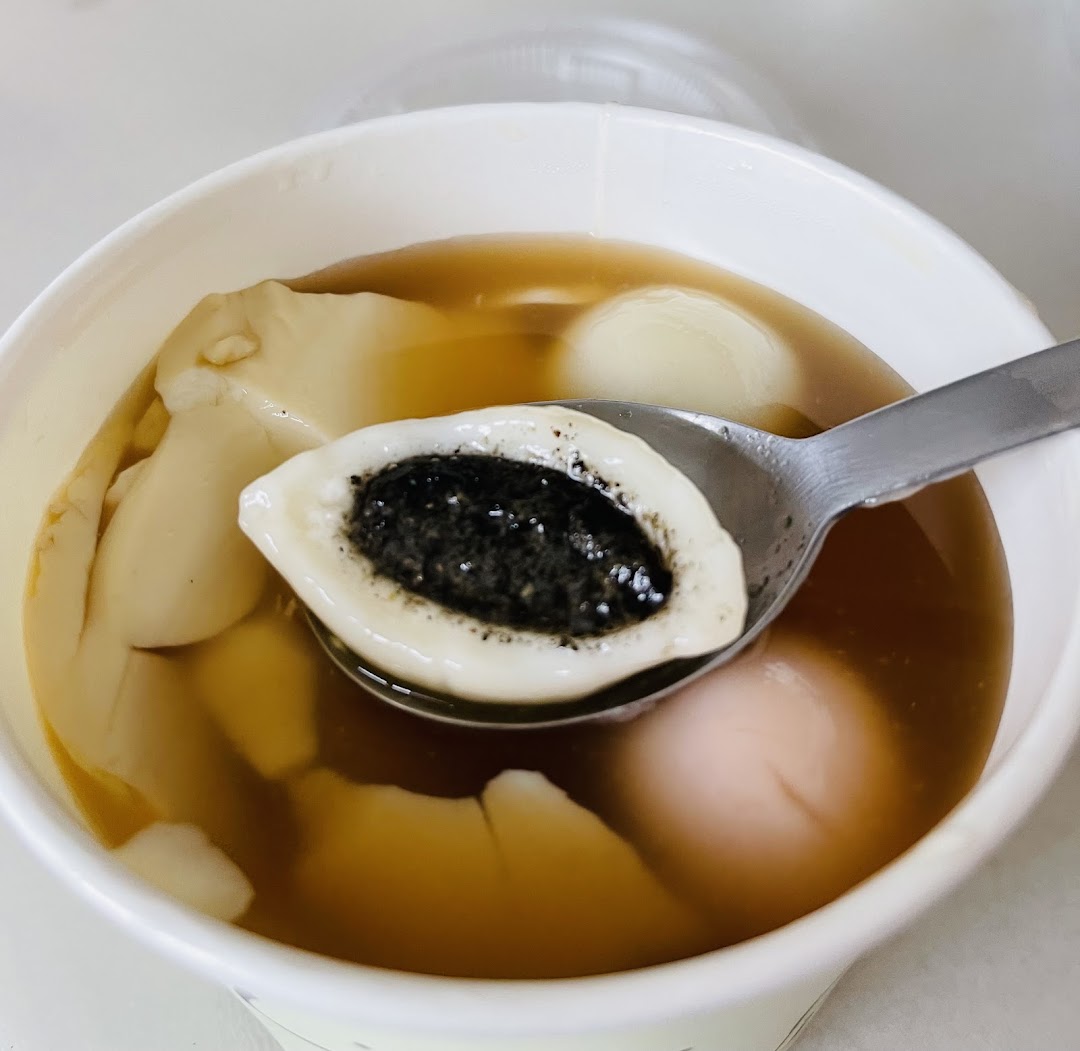 A close-up of a Mr Bean dessert featuring smooth tofu pudding and glutinous rice balls, one with black sesame filling.