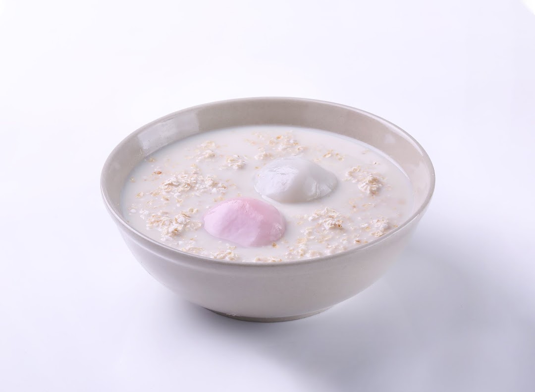 A bowl of creamy oatmeal or cereal with two colorful mochi-like dumplings.