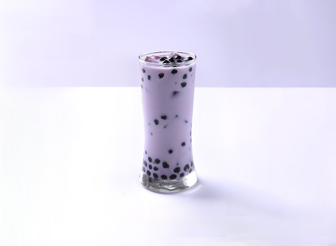 A tall glass of purple bubble tea with dark boba pearls on a white background.