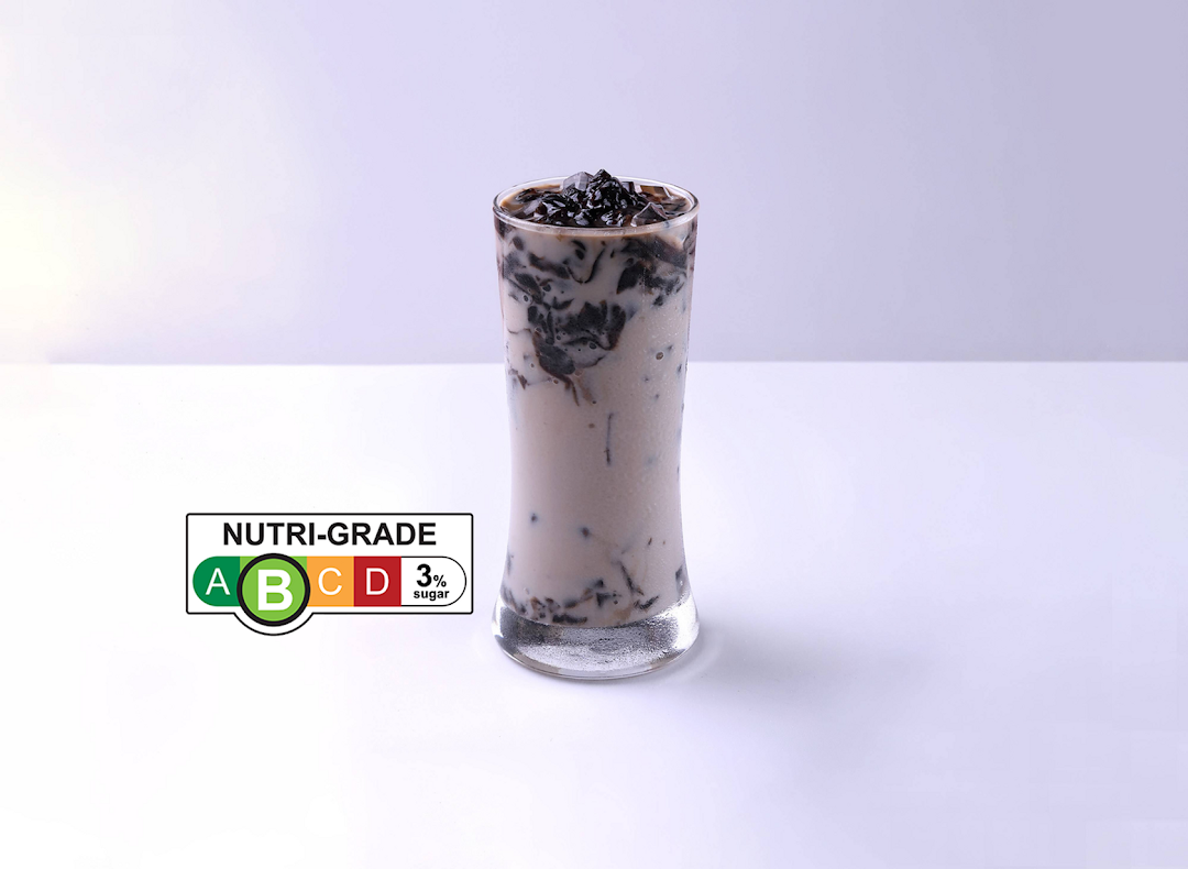 A tall glass of a milky beverage with dark jelly pieces and a 'Nutri-Grade B' label.