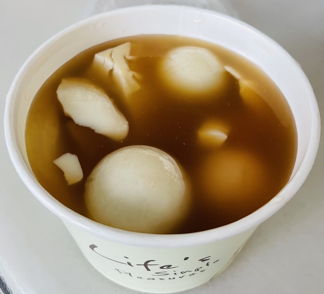 A close-up of a cup of traditional dessert soup with glutinous rice balls and beancurd.