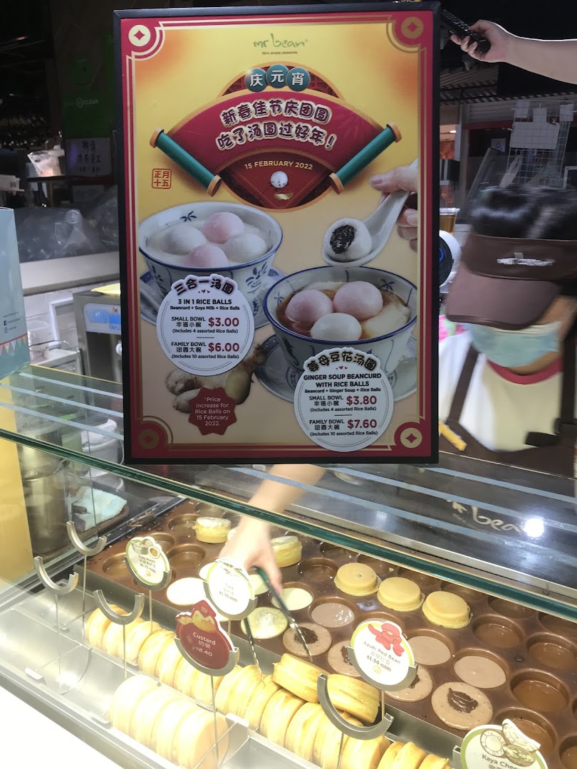 A vibrant menu board for Mr Bean featuring rice balls and beancurd, alongside a display of freshly made pastries.