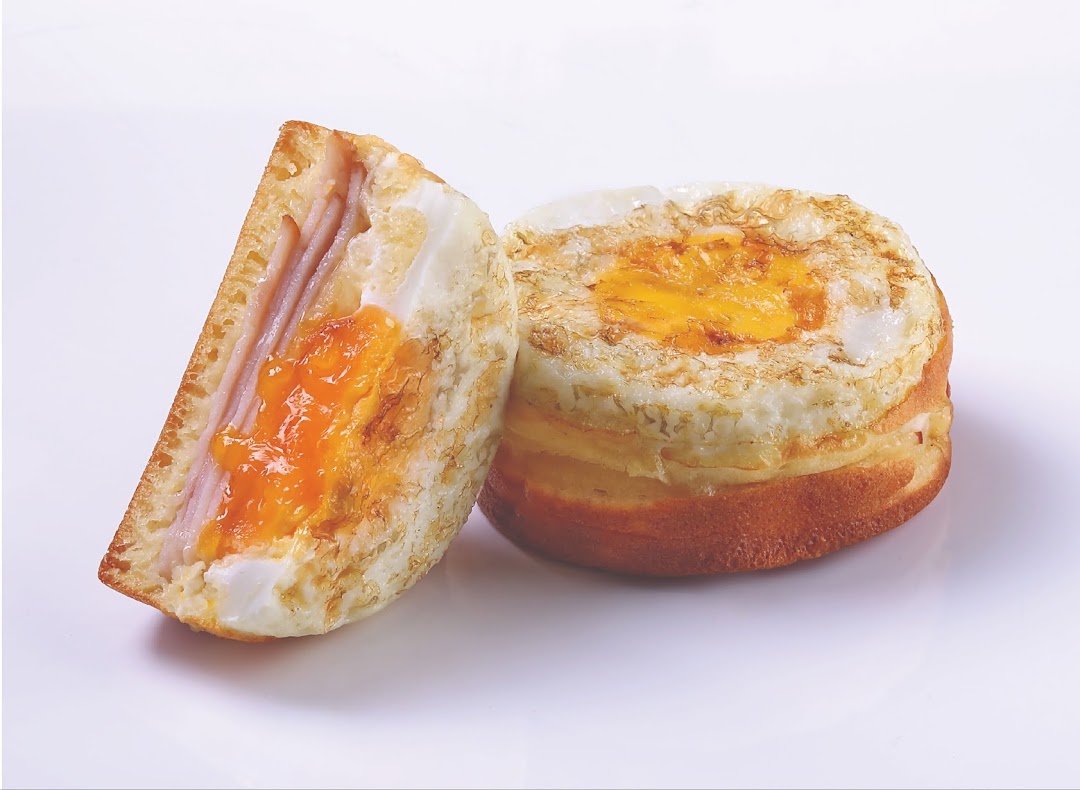 A savory bun or sandwich with ham and a fried egg, one cut in half to show the filling.