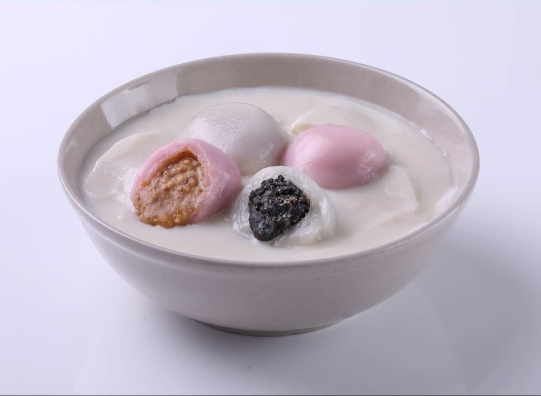 A bowl of colorful tangyuan dessert with various fillings in a creamy white soup.