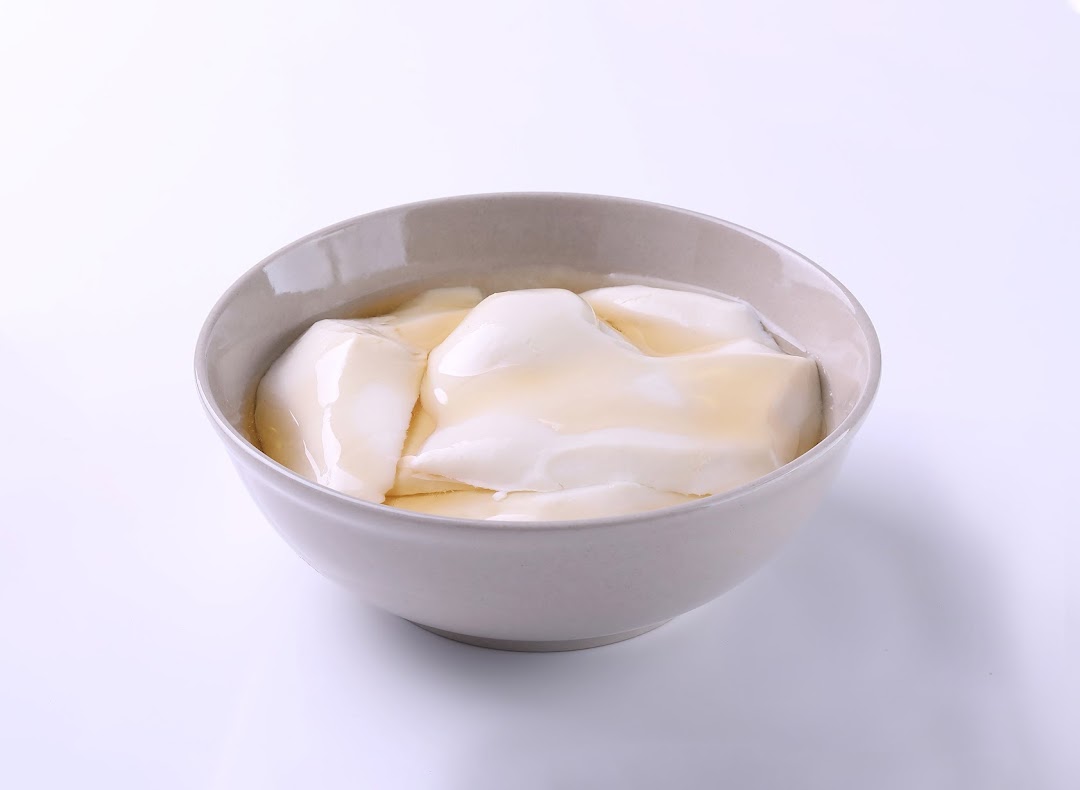 A bowl of smooth tofu pudding with a drizzle of syrup on a white background.