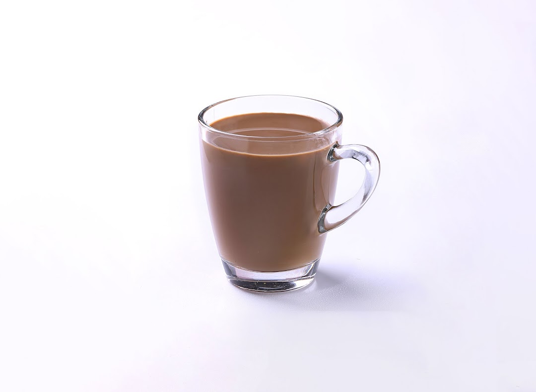 A clear glass mug filled with a light brown beverage, possibly coffee or soy milk, on a white background.
