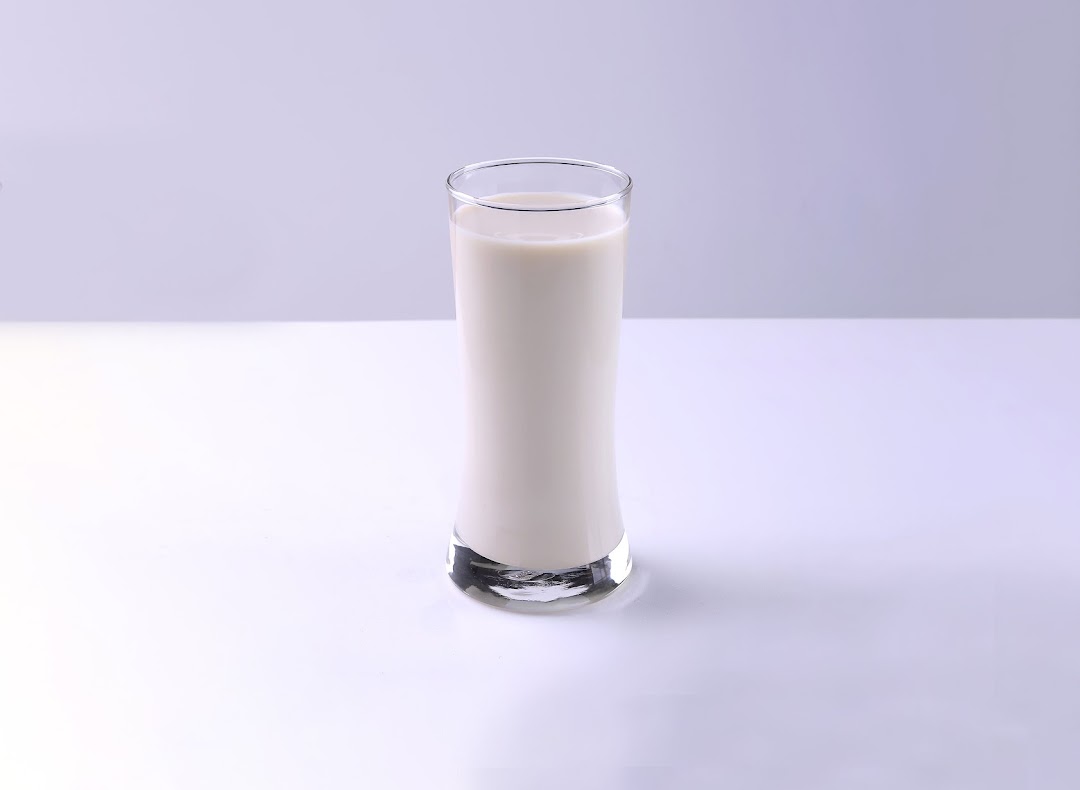 A tall glass filled with creamy white soy milk on a clean white surface.