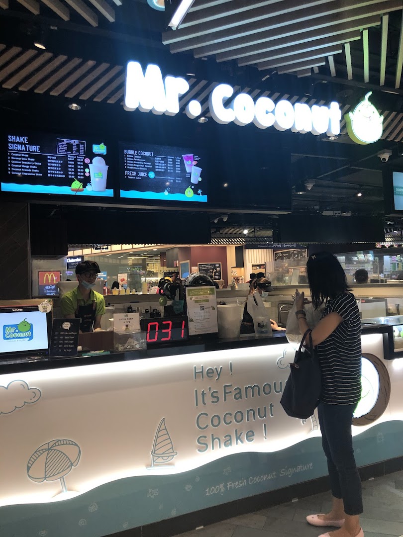 A customer at the Mr Coconut counter, with staff and digital menu boards visible.