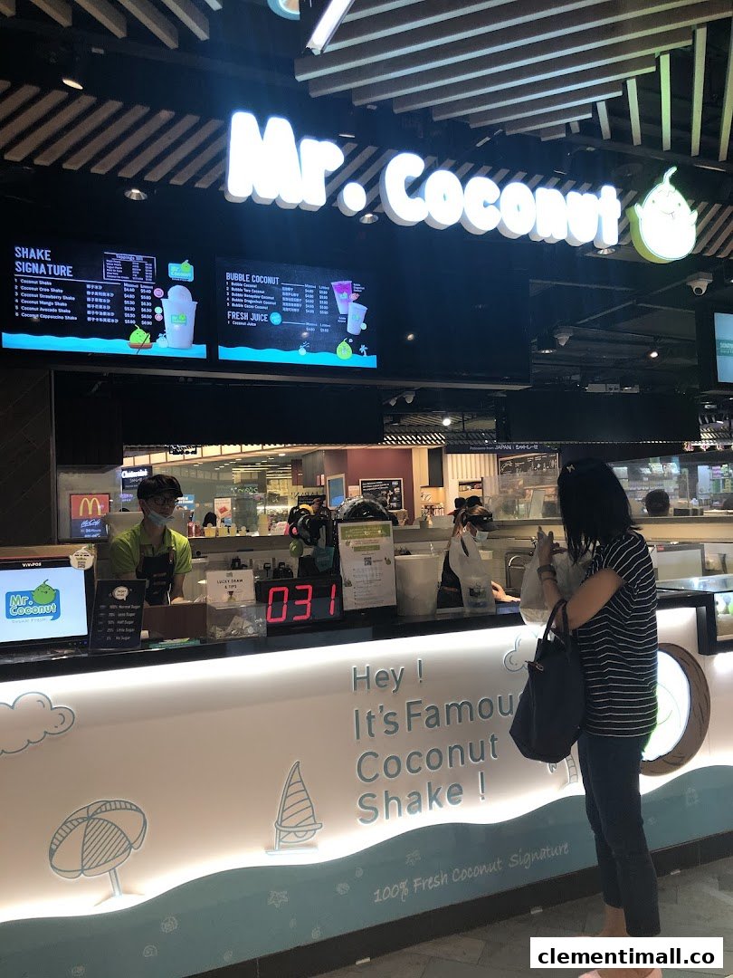 A customer at the Mr Coconut counter, with staff and digital menu boards visible.