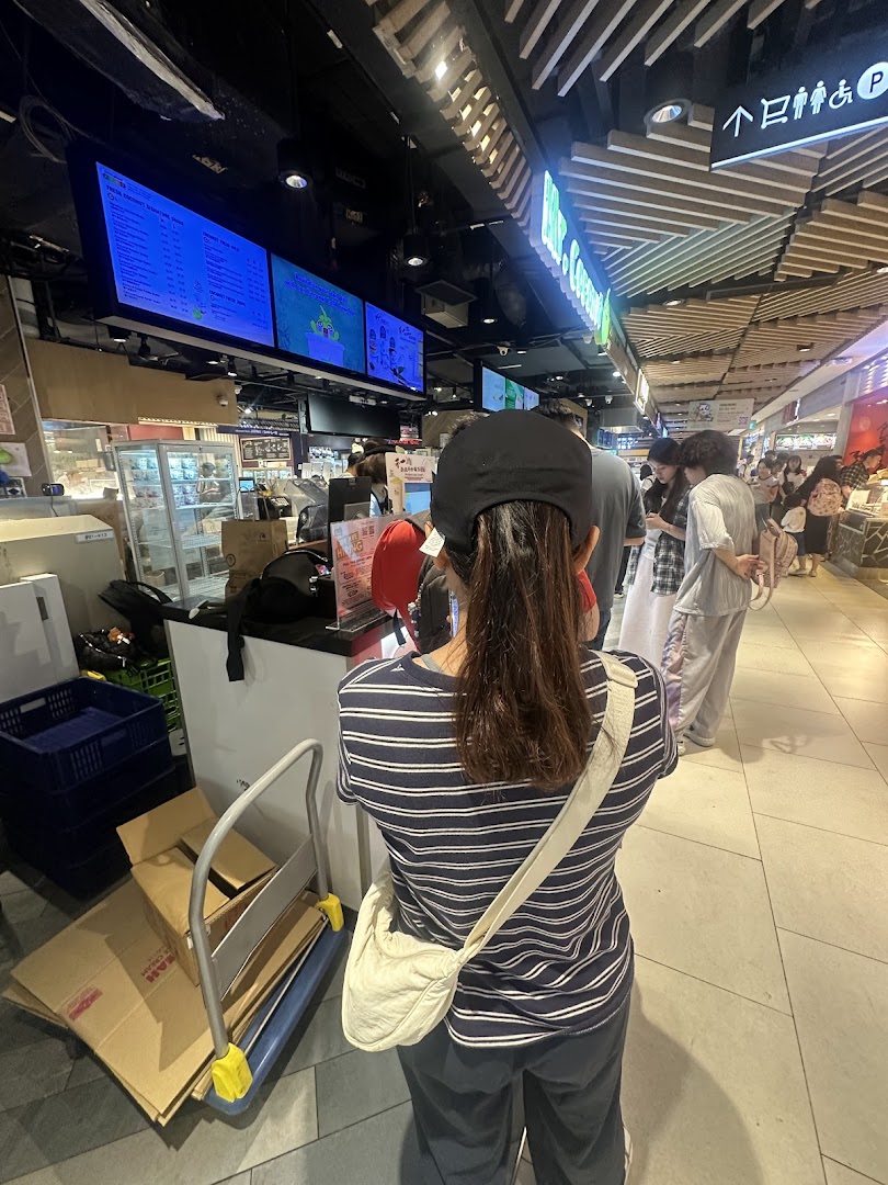 A customer queues at Mr Coconut, with digital menu screens displaying various coconut beverages.