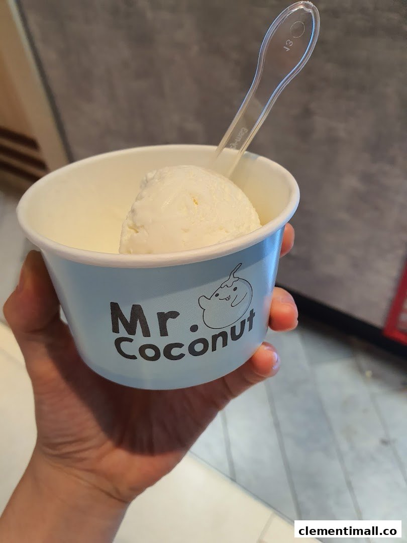 A hand holding a light blue cup of Mr Coconut ice cream with a spoon.