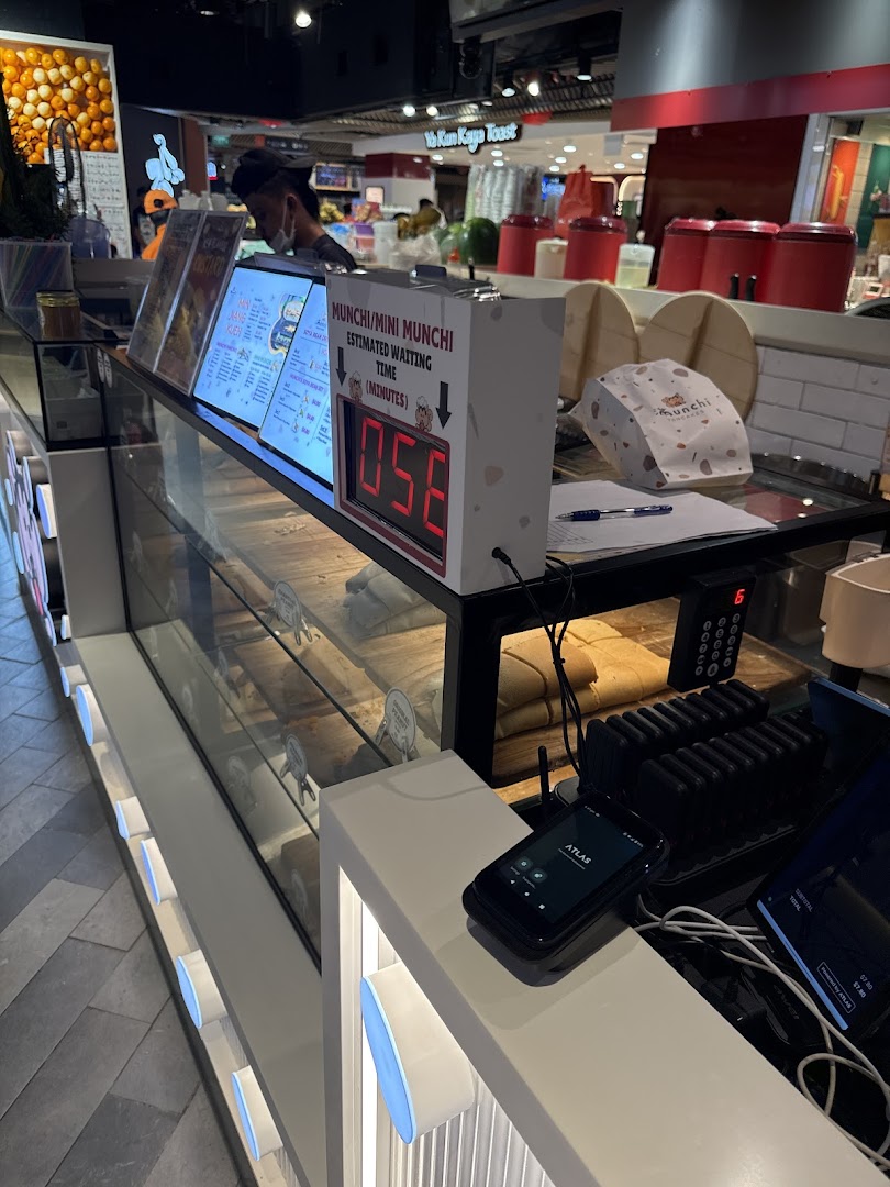 A view of the Munchi Pancakes counter, showcasing their display case, menu boards, and a waiting time display.