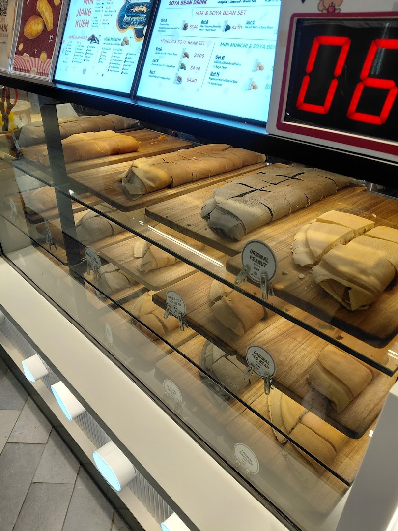 A vibrant display case showcasing various freshly made Munchi pancakes and a digital menu board.