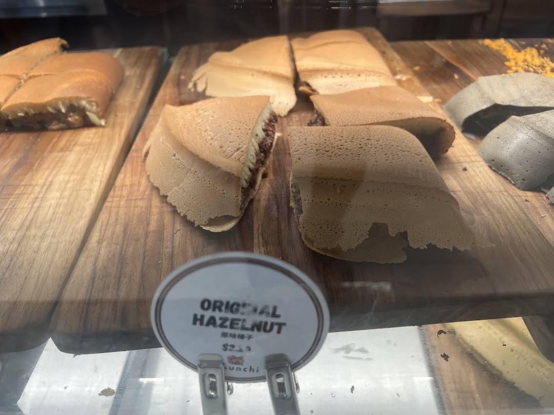 Close-up of various Munchi Pancakes, including Original Hazelnut, displayed on wooden boards in a glass case.