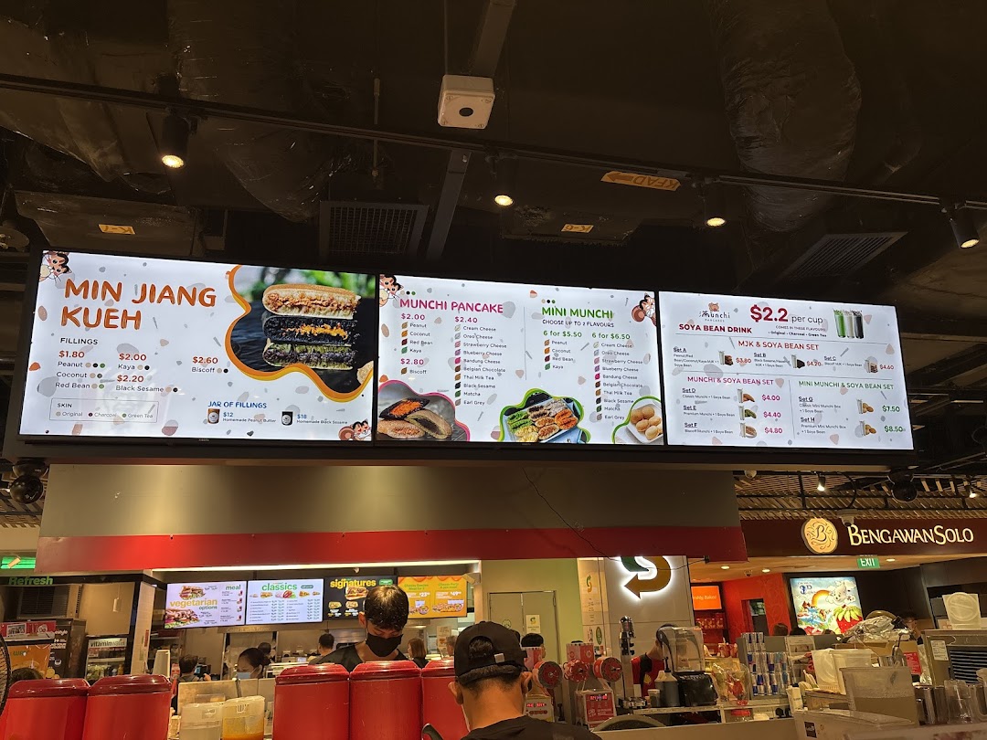 A brightly lit digital menu board for Munchi Pancakes, displaying various pancake and soya bean drink options.
