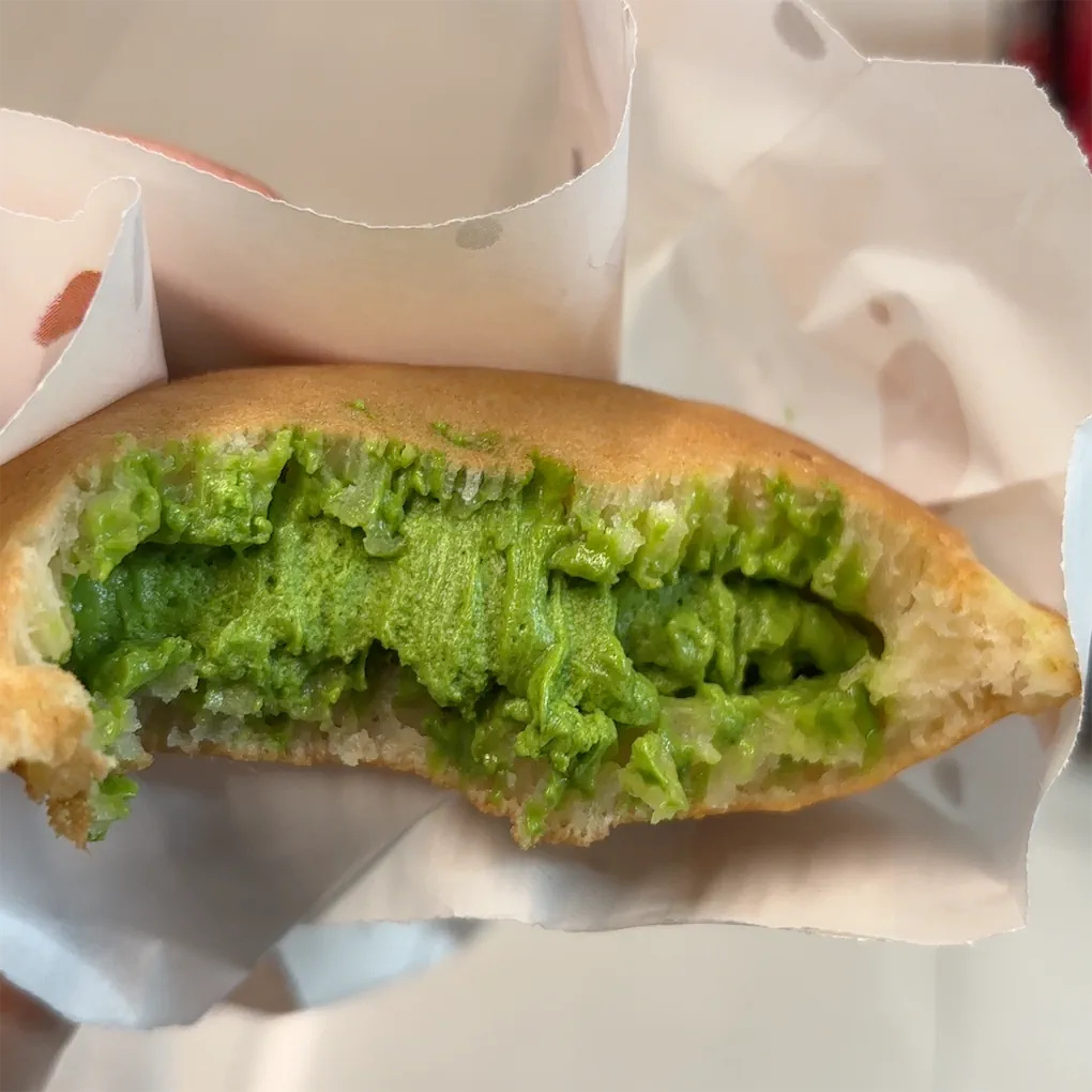 A close-up of a Munchi pancake filled with vibrant green matcha cream, held in white paper packaging.