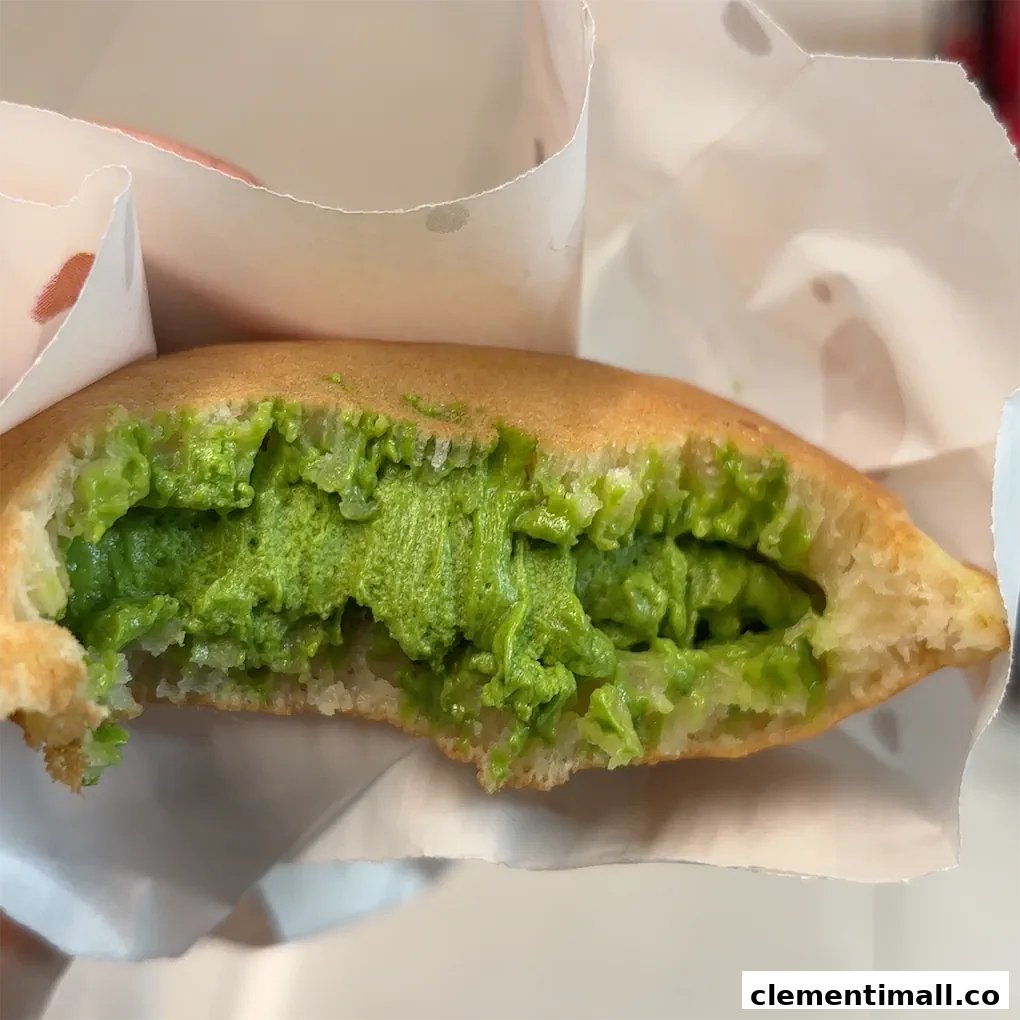 A close-up of a Munchi pancake filled with vibrant green matcha cream, held in white paper packaging.