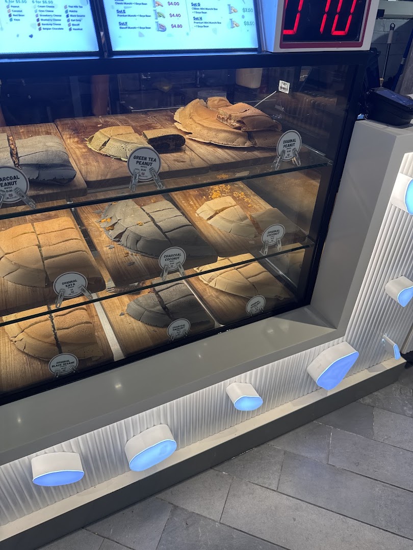 A vibrant display case showcasing various Munchi Pancakes like Charcoal Peanut, Green Tea Peanut, and Original Kaya.