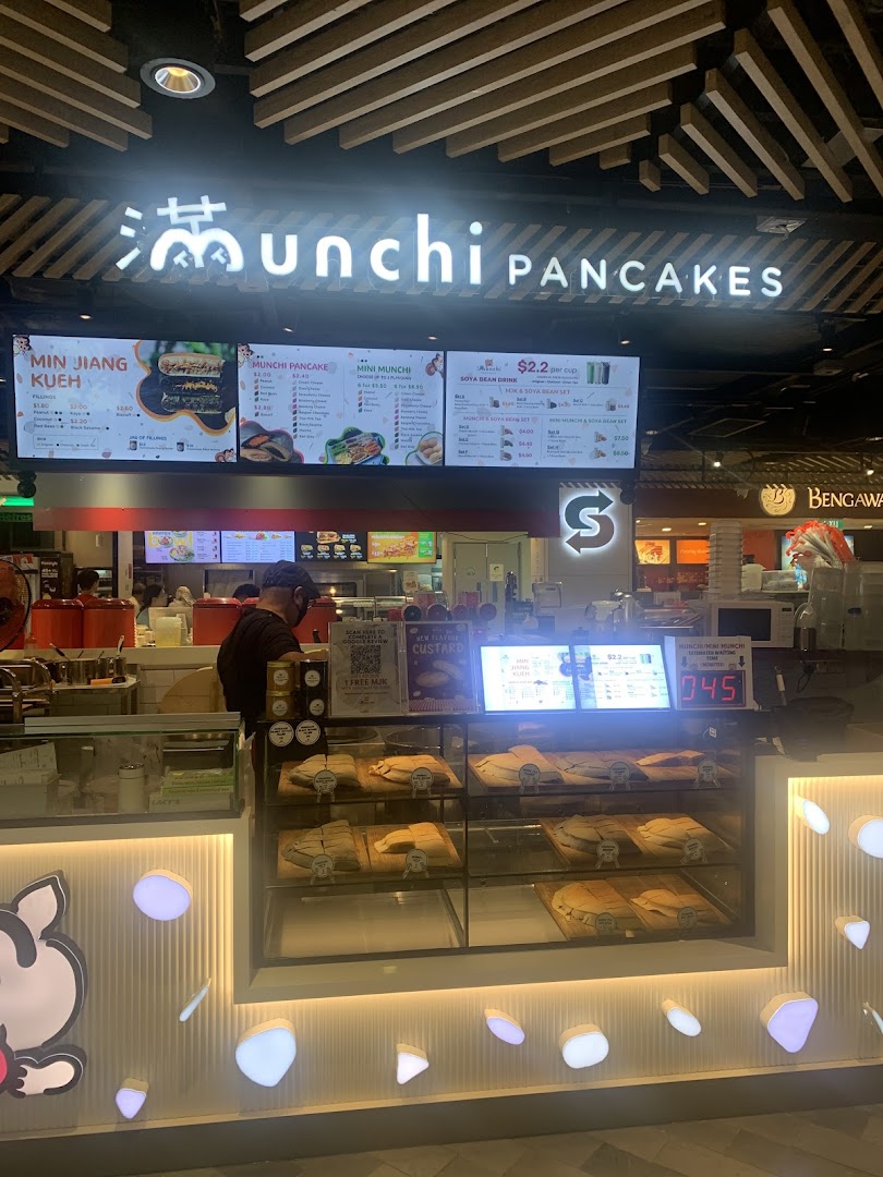 A brightly lit Munchi Pancakes shop front showcasing its digital menu board and fresh pancake display.