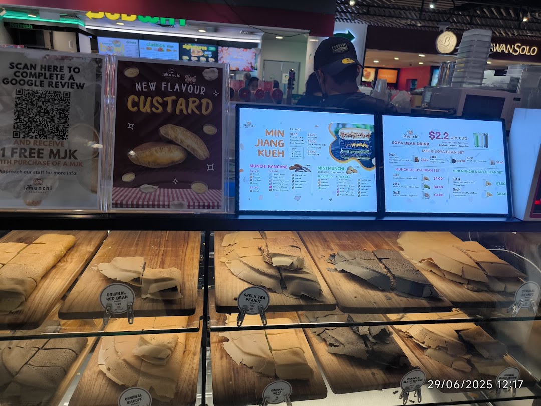 A display counter at Munchi Pancakes showcasing various pancakes and digital menu screens with prices.