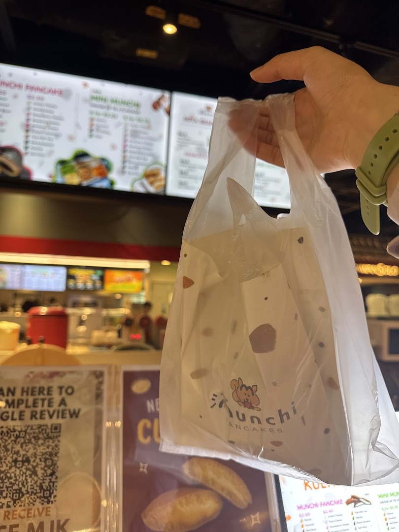 A customer holds a Munchi Pancakes takeaway bag inside the vibrant shop, with menu boards visible.