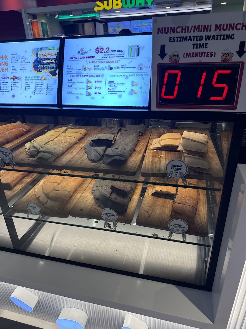 A display case showcasing various Munchi pancakes with digital menu boards and a waiting time display.