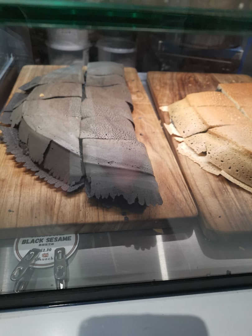 Close-up of black sesame and traditional pancakes displayed on wooden boards in a glass case.
