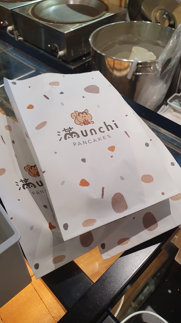 Branded takeaway bags from Munchi Pancakes with cooking equipment visible in the background.