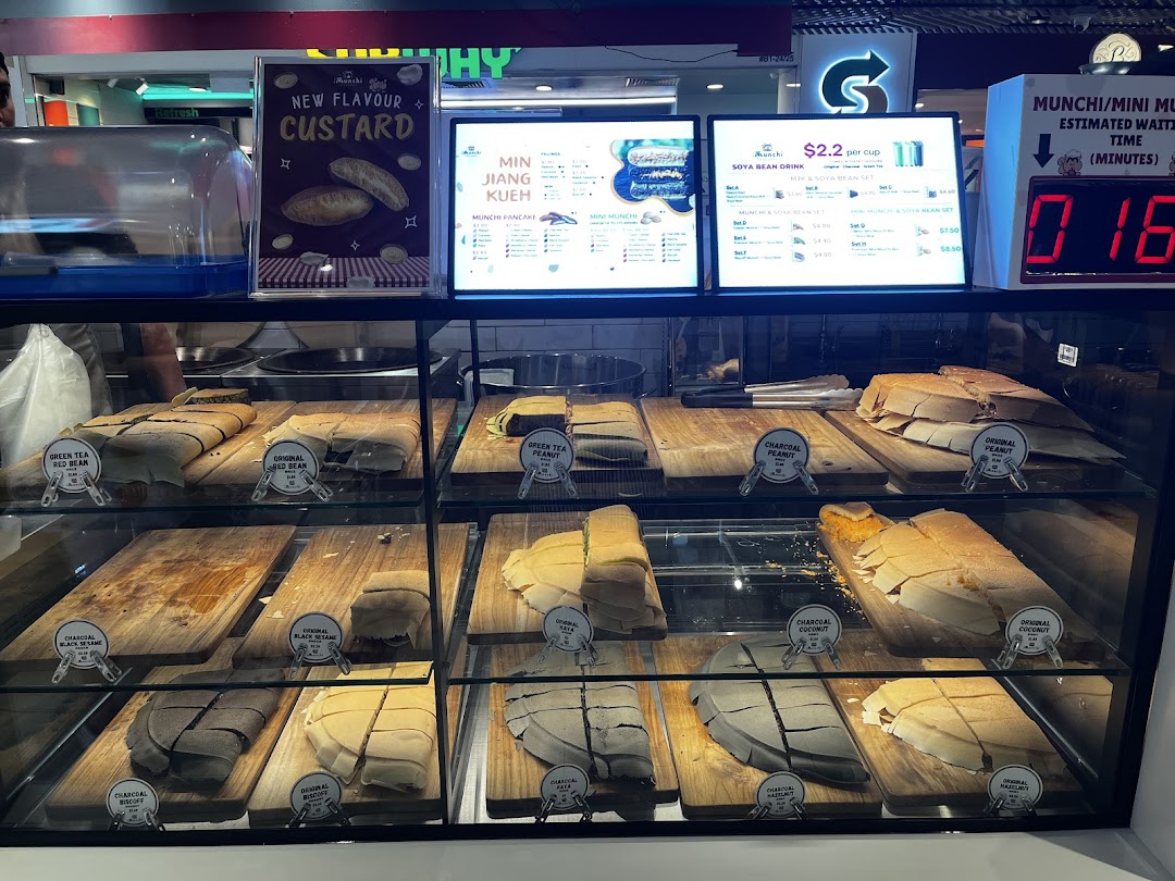 A vibrant display counter showcasing various Munchi Pancakes and digital menu boards with prices.