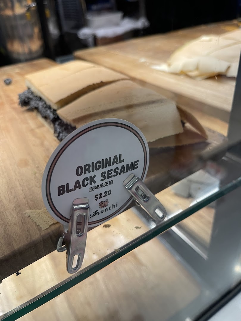 A close-up of Munchi Pancakes' Original Black Sesame pancake with its price tag on a wooden display.