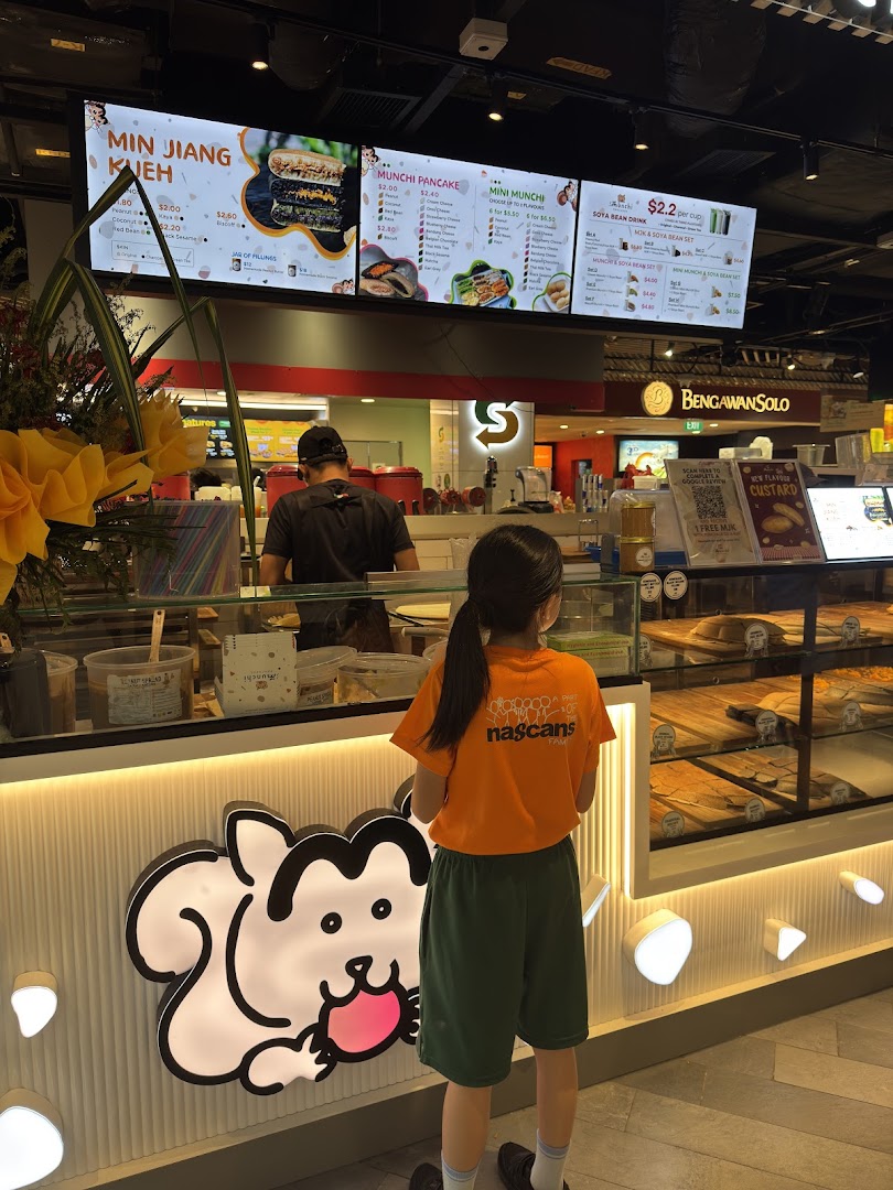 A customer stands at the counter of Munchi Pancakes, with digital menu boards displaying various pancake and drink options.