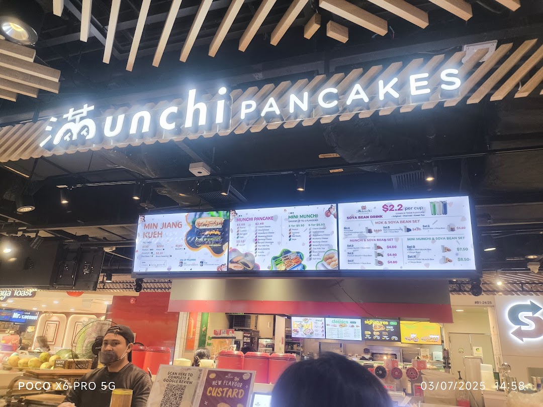 A vibrant shot of Munchi Pancakes' counter, featuring their bright digital menu board and a staff member.