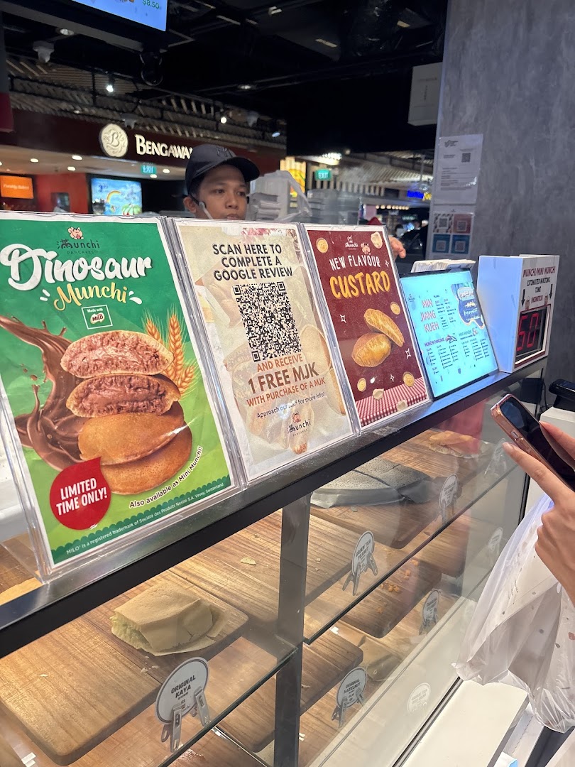 A staff member stands behind the counter of Munchi Pancakes, showcasing promotional displays and a product display case.