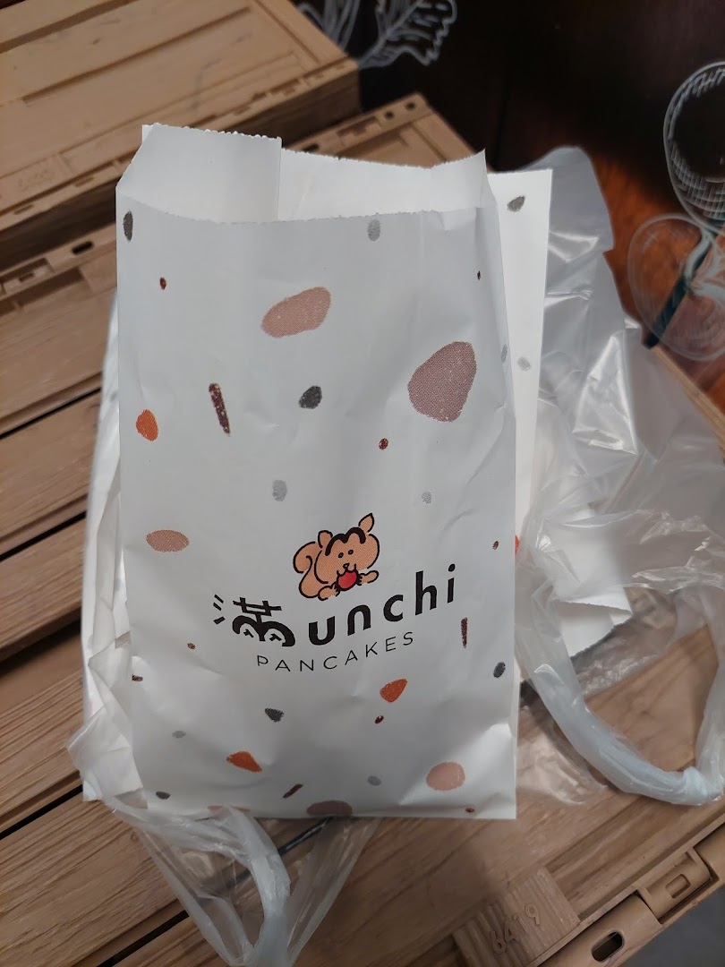 A white paper bag from Munchi Pancakes featuring a cute squirrel logo and colorful speckles.